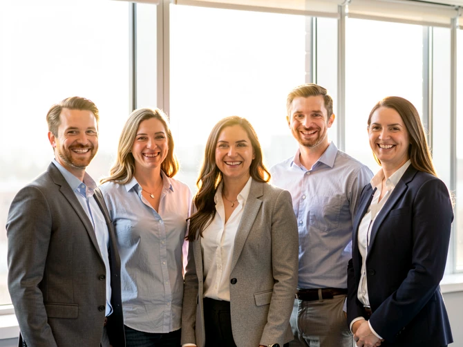 A group of five colleagues standing in a row against a bright office window, all smiling at the camera, each person clearly separated with distinct facial features visible. Soft natural daylight from the window behind creates a gentle rim light on their shoulders. Style: corporate team photography. Mood: friendly and professional.
